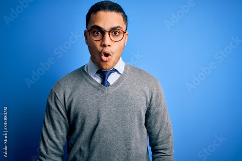 Young brazilian businessman wearing tie standing over isolated blue background afraid and shocked with surprise expression, fear and excited face.