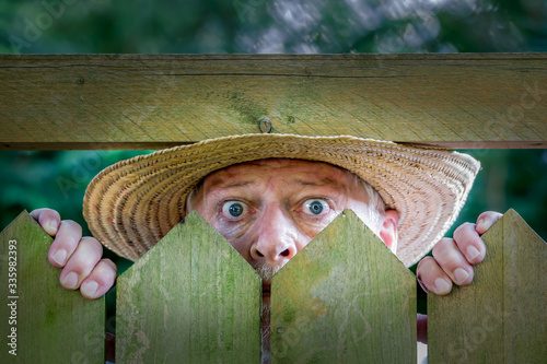 Foto An elderly man in a straw hat looks curiously over a garden fence