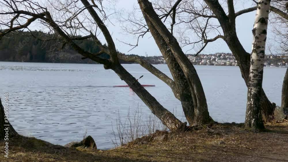 Man kayaking alone in the river behind trees with city in background Man kayaking alone in the river behind trees with city in background