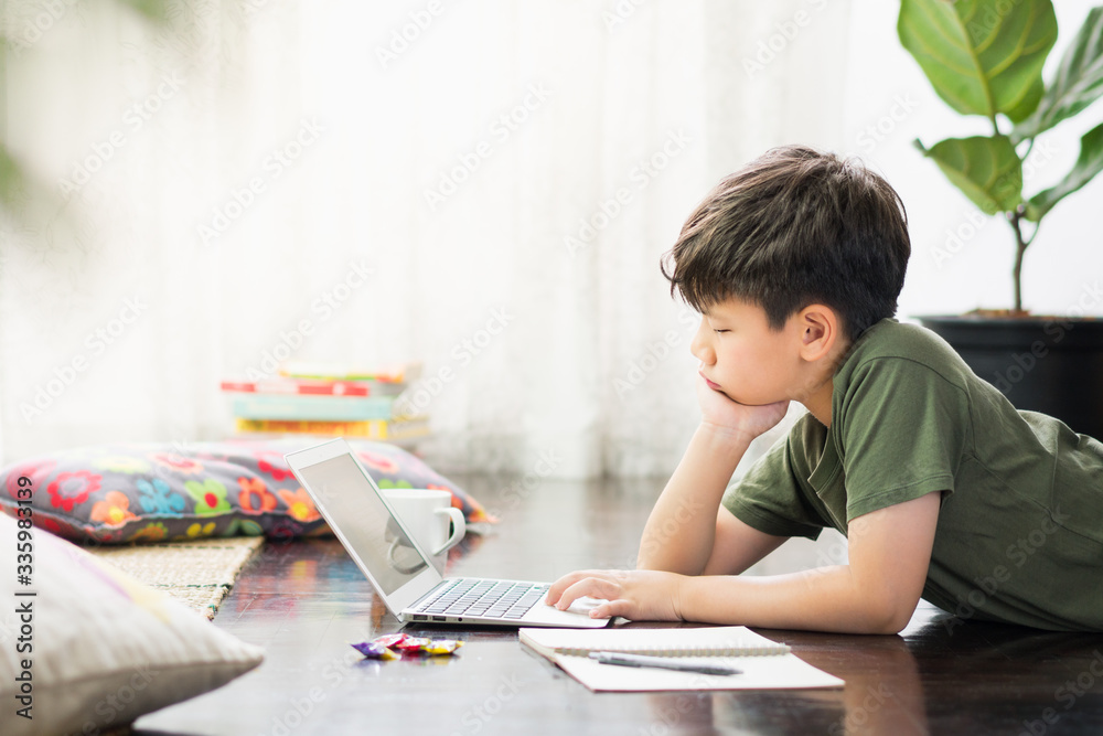 Smart looking Asian preteen boy use laptop computer at home study lessons through online learning, feeling tired with homework due to Covid-19 pandemic and social distancing measures Smart looking Asian preteen boy use laptop computer at home study lessons through online learning, feeling tired with homework due to Covid-19 pandemic and social distancing measures