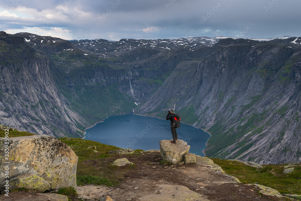 A man standing on rock and taking picture of mountain and fjord at Trolltunga, Norway, Scandinavia