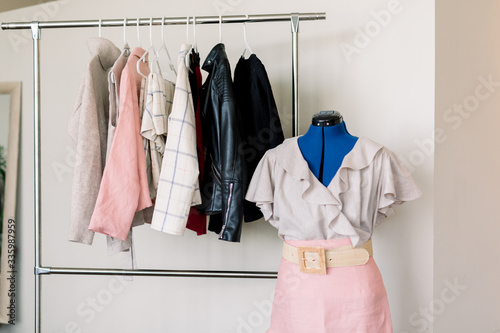 A mannequin wearing a pink skirt and ruffly blouse next to clothes hanger. photo