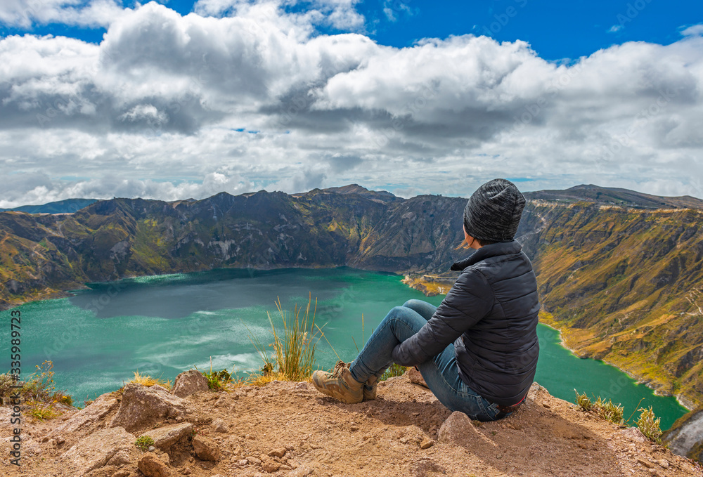 Female tourist and backpacker looking at the view of the turquoise waters of the active Quilotoa crater lake during the Quilotoa Loop hike near the city of Quito, Ecuador.