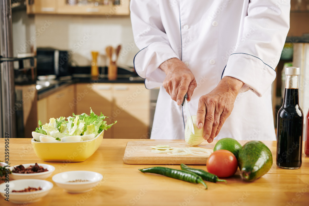 Cropped image of man in chef coat cutting onion when cooking at home