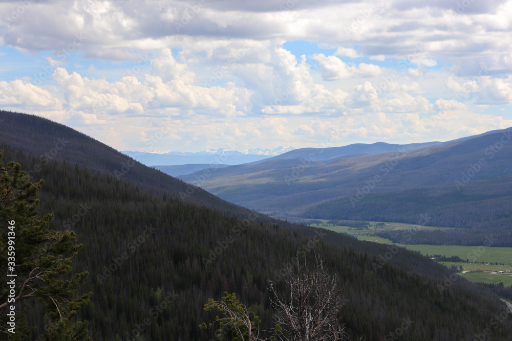 A view of the grassy covered Colorado mountains and blue cloudy skies 