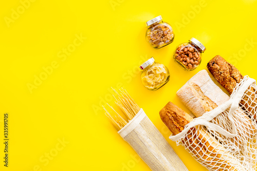 Eco bag, glass jars on yellow background, top view. Zero waste food storage concept. Copy space
