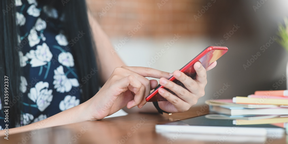 Obraz premium Cropped image of beautiful woman hands using/holding a smartphone while sitting at the wooden working desk. Woman with relaxing time concept.