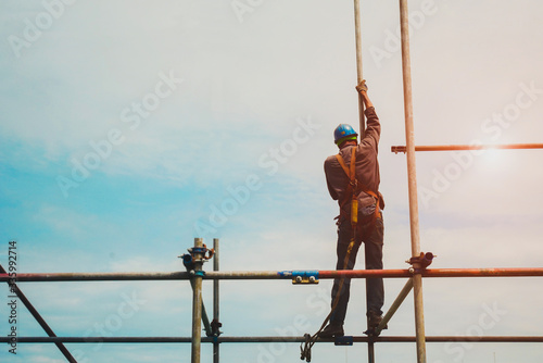 Worker on upland or high place standing on scaffolding for installed staging for safety concept wearing equipment protective full safety belt in construction site with copy space.