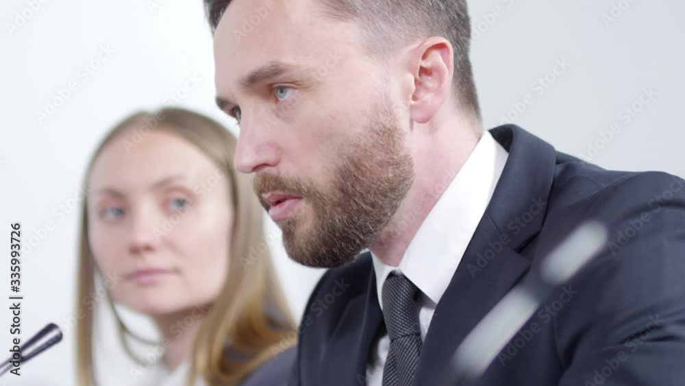 Close up of young handsome businessman speaking into microphone while holding press conference with female colleague Close up of young handsome businessman speaking into microphone while holding press conference with female colleague