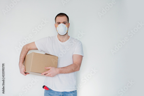 Caucasian man wearing respirator with cardboard box on a white background. Delivery man