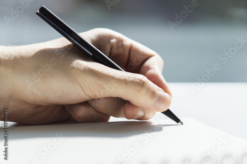 Man writes with a pen in notepad in a sunny office, business and education concept. Close up