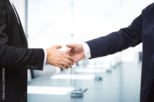 Two businessmen shake hands on the background of sunny meeting room, deal concept, close up