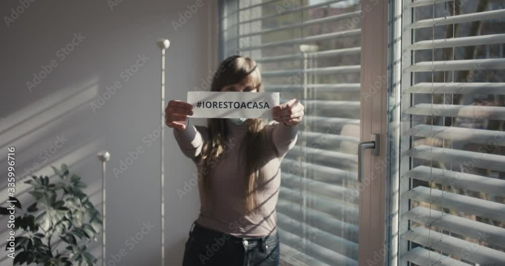 Woman with protective face mask shows Italian stay home sign during coronavirus covid 19 pandemic outbreak social distancing self isolation in quarantine