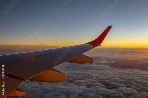 Aircraft wing with fluffy clouds below and orange horizon during sunset