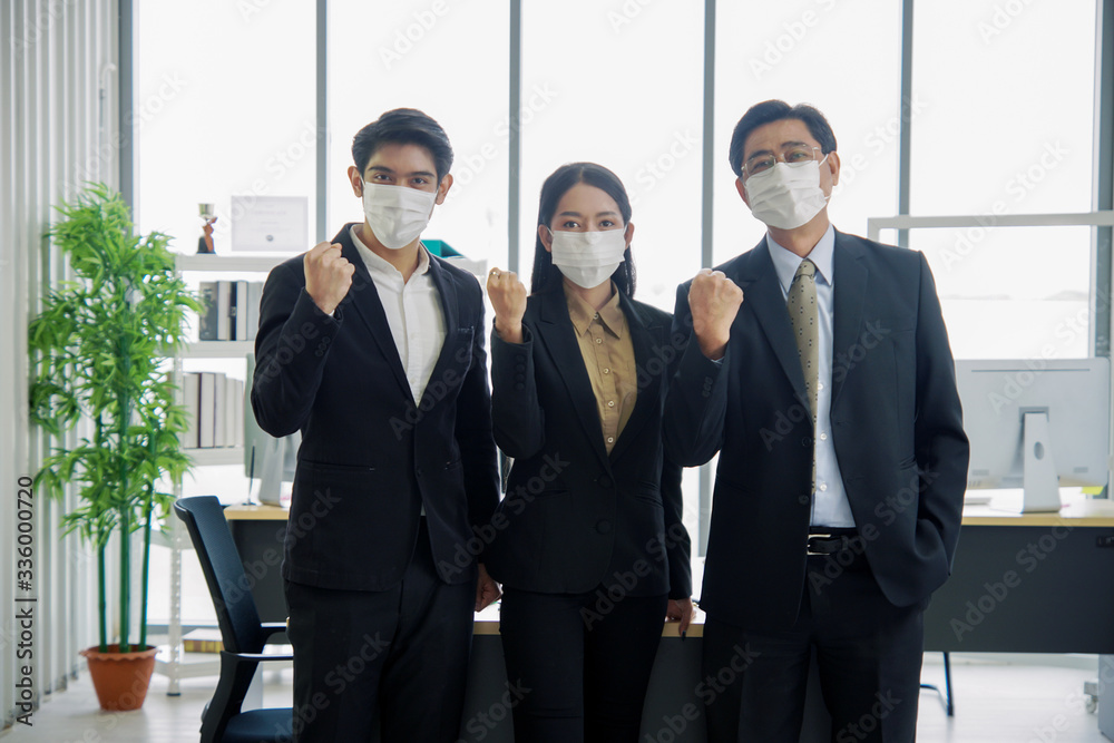 Asian businessmen and businesswoman are wearing a mask at workplace to prevent the corona virus outbreak. They held their fists to mean we would fight and pass it together. Asian businessmen and businesswoman are wearing a mask at workplace to prevent the corona virus outbreak. They held their fists to mean we would fight and pass it together.