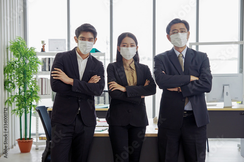Asian businessmen and businesswoman are wearing a mask at workplace to prevent the corona virus outbreak. © Pruksachat
