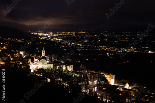 Aerial view of Assisi town (Umbria, Italy) and valley at night, with city lights and Santa Chiara church