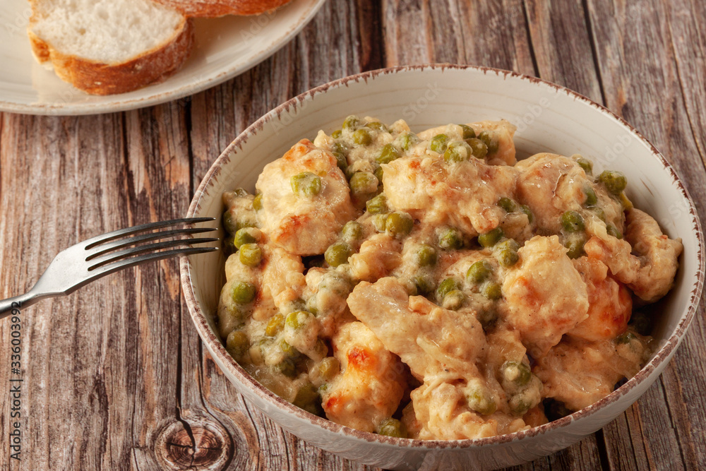 Chicken fillet with green peas stewed in a creamy sauce on a wooden table