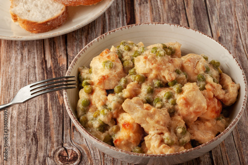 Chicken fillet with green peas stewed in a creamy sauce on a wooden table