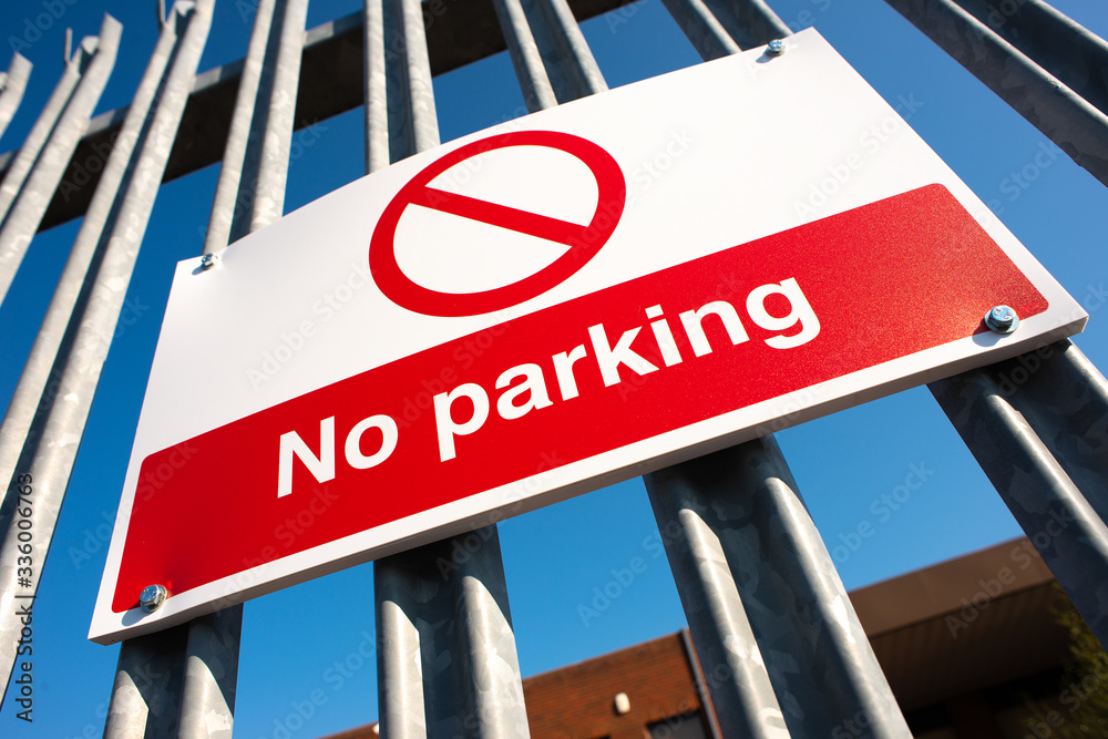Obraz premium Low angle view, of a red & white No Parking sign attached to a metal security fence, at an industrial trading estate in Colliers Wood, London, UK