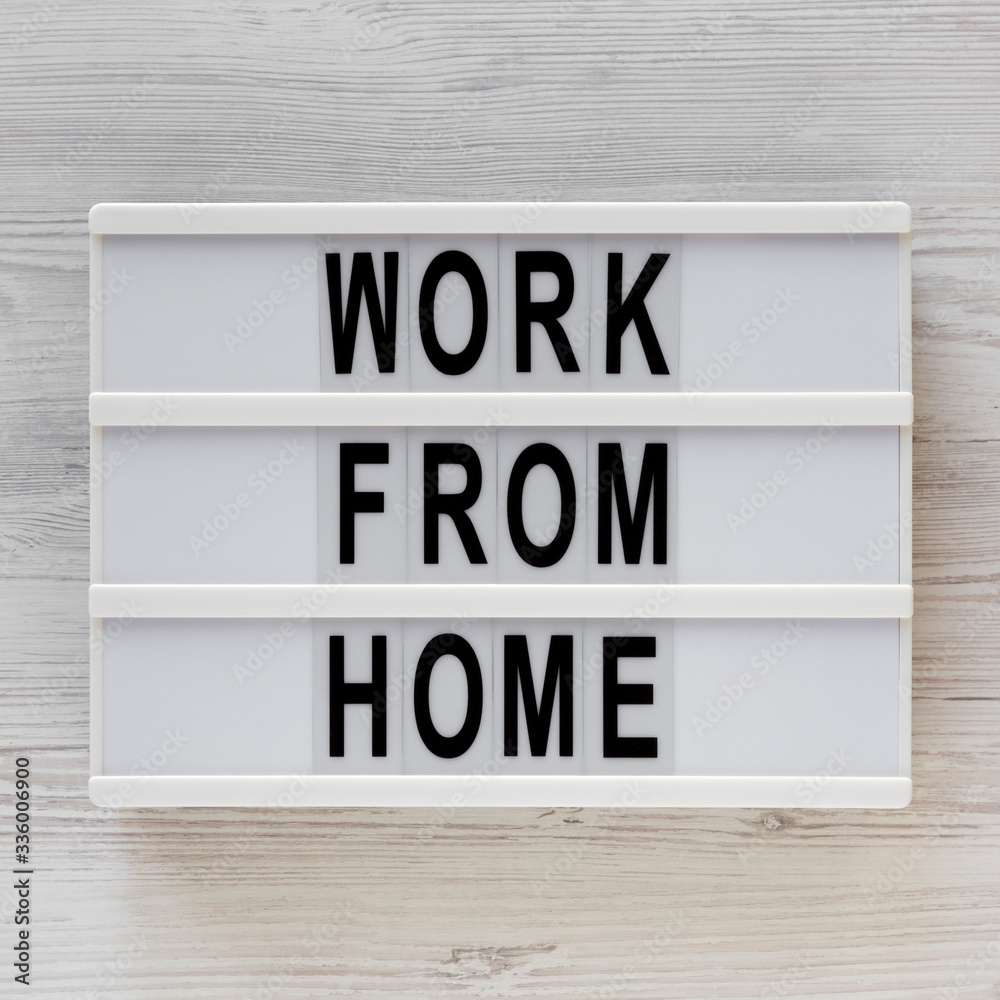 'Work from Home' words on a lightbox on a white wooden surface, top view. Overhead, from above, flat lay.