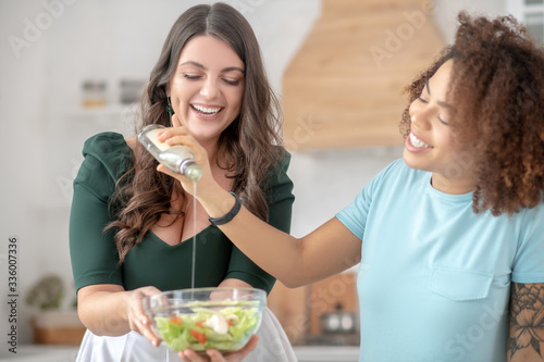 Two women add salad oil in vegetable salad.