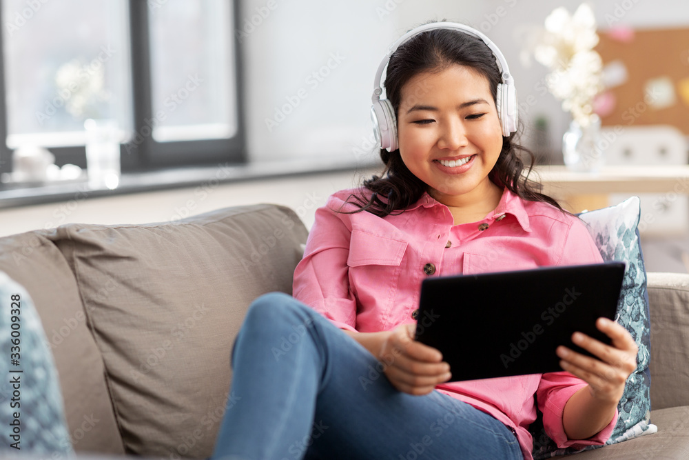 people and leisure concept - happy smiling asian young woman in headphones listening to music on tablet pc computer at home people and leisure concept - happy smiling asian young woman in headphones listening to music on tablet pc computer at home