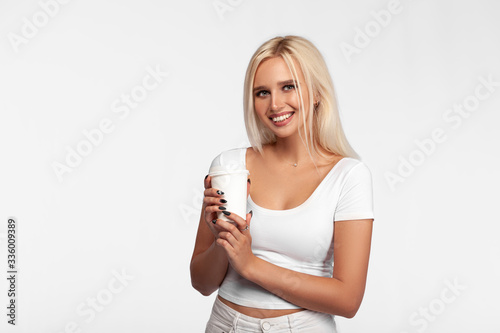 Young blonde woman over isolated white background holding cup of coffee. Portrait of girl in white t-shirt with cup of tea. Mockup.