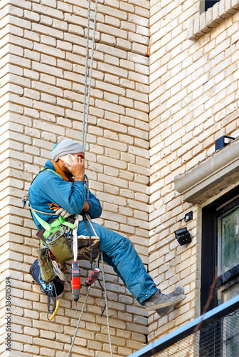 Wallpaper Mural Builder climber hanging on safety ropes on the wall of an old brick building with tools tied to himself and talking on a cell phone. Torontodigital.ca