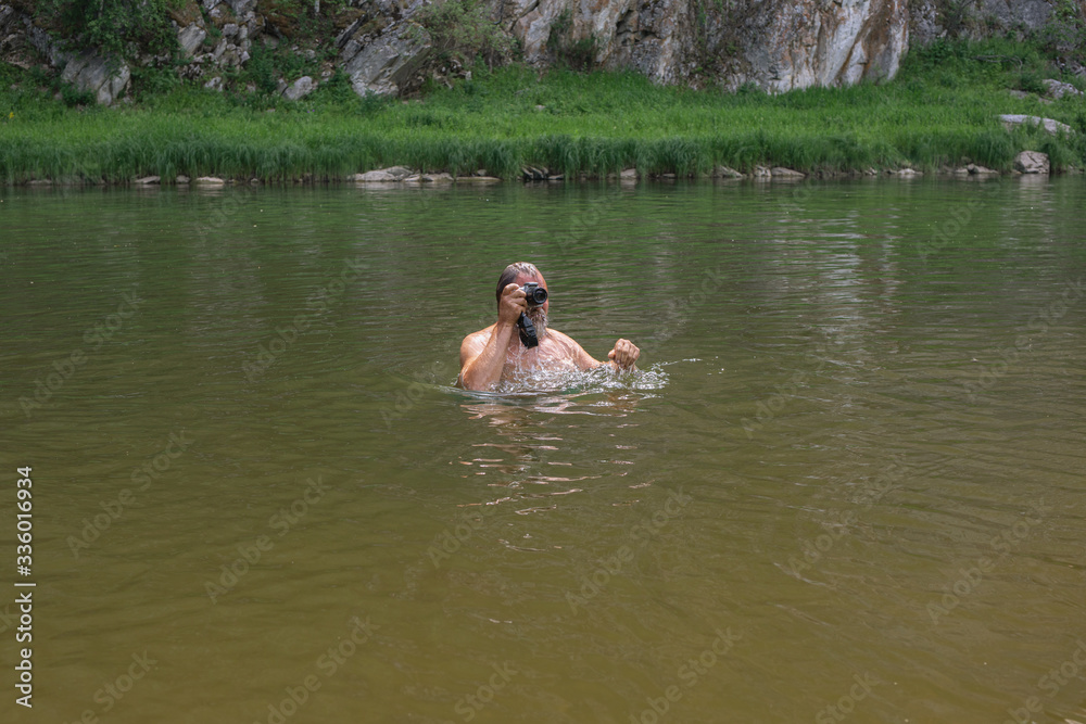 man aged plunged into the water looking or peeping through waterproof camera. Professional photographer job concept. Work in difficult conditions.