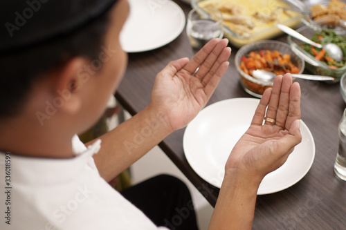 young man with muslim cap pray open his arm before having the meal