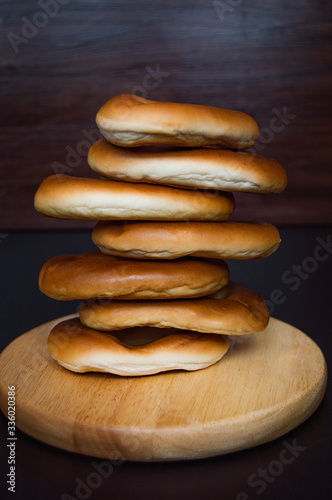 A lot of oval bagels on a wooden stand on the dark background.