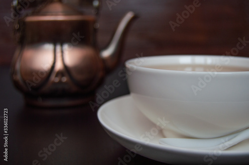 White tea cup with saucer and tea spoon on dark background.