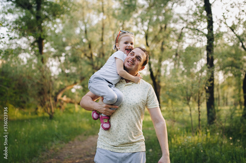 A young, loving male dad in a tracksuit holds a small, beautiful and smiling girl daughter in his arms on the nature in the park and have fun together. Photography, concept.