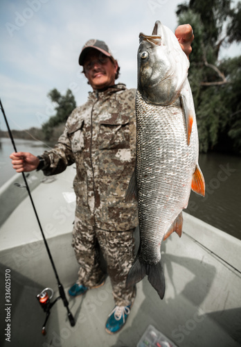 Angler stands in the boat and holds the trophy Asp fish