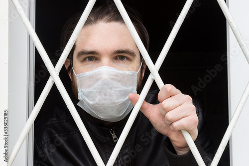 male model in a disposable mask, dark hair, beard and leather jacket.A coronavirus patient remains at home under quarantine and disease prevention, but wants to escape from house arrest.