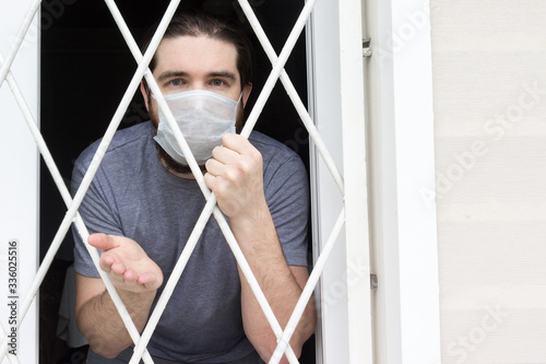 male model in a disposable mask, dark hair, beard and grey t-shirt.A coronavirus patient remains at home under quarantine and disease prevention.Sad and negative Emotions in the eyes of a person