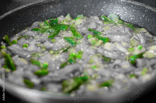 Black and white photo of frozen vegetables in a pan with highlighted green asparagus.