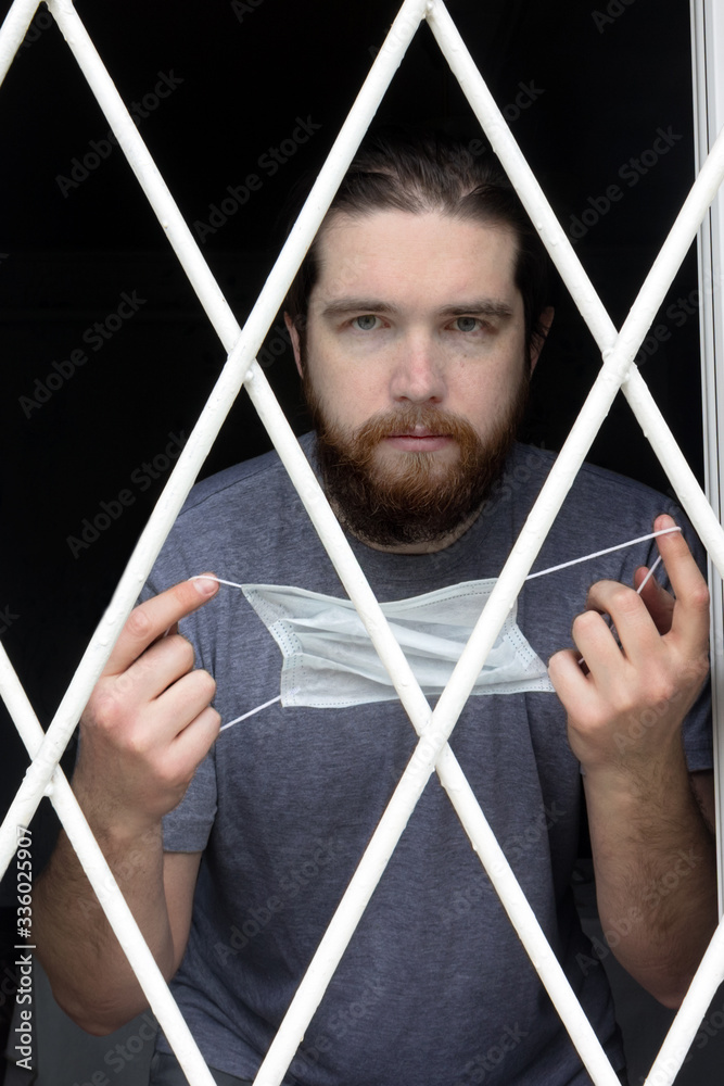 male model in a disposable mask, dark hair, beard and grey t-shirt.A coronavirus patient remains at home under quarantine and disease prevention.Sad and negative Emotions in the eyes of a person male model in a disposable mask, dark hair, beard and grey t-shirt.A coronavirus patient remains at home under quarantine and disease prevention.Sad and negative Emotions in the eyes of a person