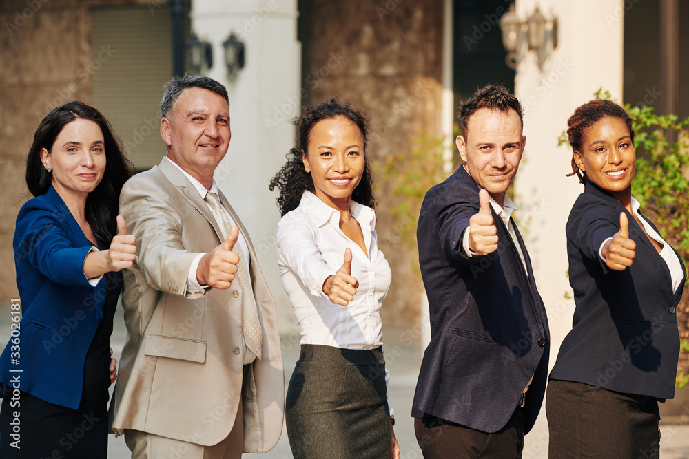 Excited successful multi-ethnic business team standing outdoors and showing thumbs-up Excited successful multi-ethnic business team standing outdoors and showing thumbs-up