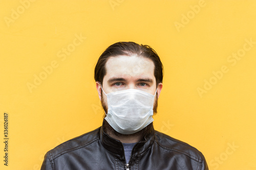male model in a disposable mask, dark hair, beard and leather jacket. Yellow background.Model for advertising coronavirus and protective equipment