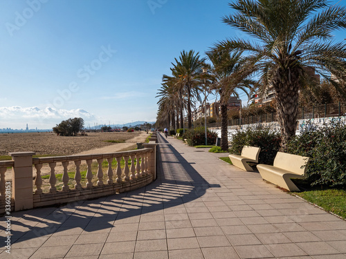 Promenade seafront in Masnou, Catalonia, Spain near Barcelona. Attractive walking zone along the beach and sea. Famous tourist destination in Spain. Palms and stone benches on sunny day.