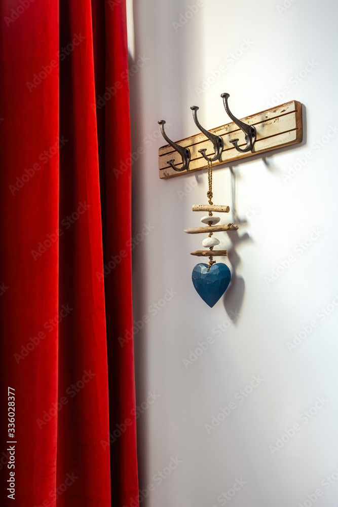 Wooden vintage style hanger with decorative blue heart and red curtain. Hooks on a wall at an entrance to home.
