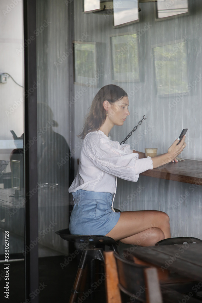 Woman in cafe drinking coffee and using her mobile phone Woman in cafe drinking coffee and using her mobile phone