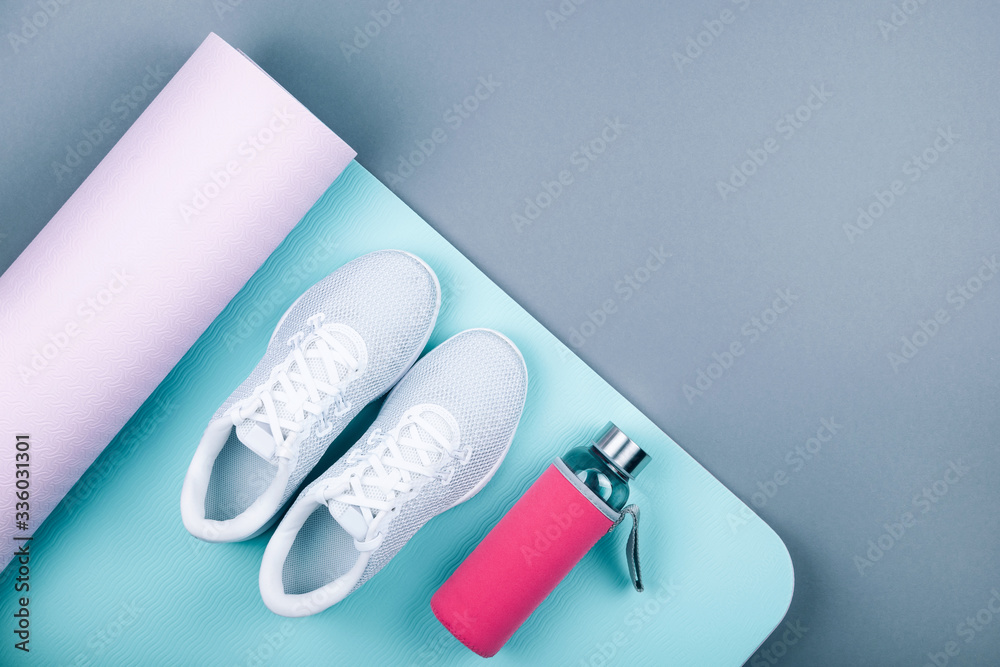 Naklejka premium Top view of white sport shoes sneakers blue pink yoga mat,glass water bottle on pastel grey background. Yoga pilates or fitness practice. Losing weight and sport concept. Flat Lay.