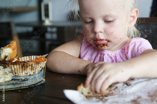 Candid portrait of a toddler girl eating chocolate cake. Happy childhood concept.
