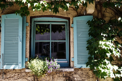 Fenster mit Blumenschmuck blauem Rahmen und blauem Fensterladen und Spiegelung im Glas