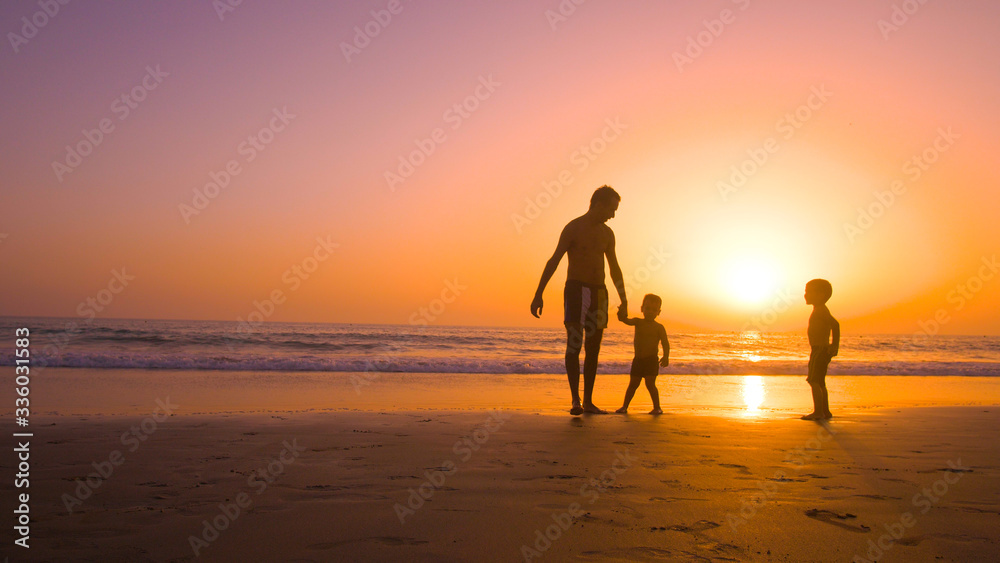 Father with kids playing in the beach at sunset