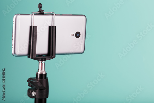 The smartphone is mounted on a tripod as a photo-video camera for a blog on a blue background. Record videos and photos.