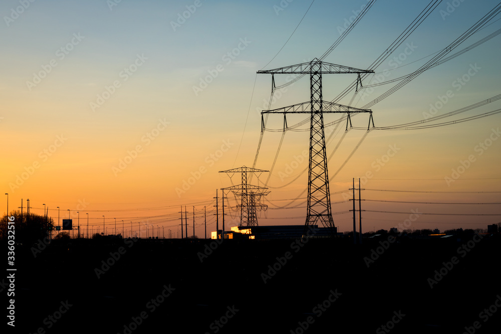 High-voltage pylons with power lines for the transport of electricity are outlined against the twilight sky